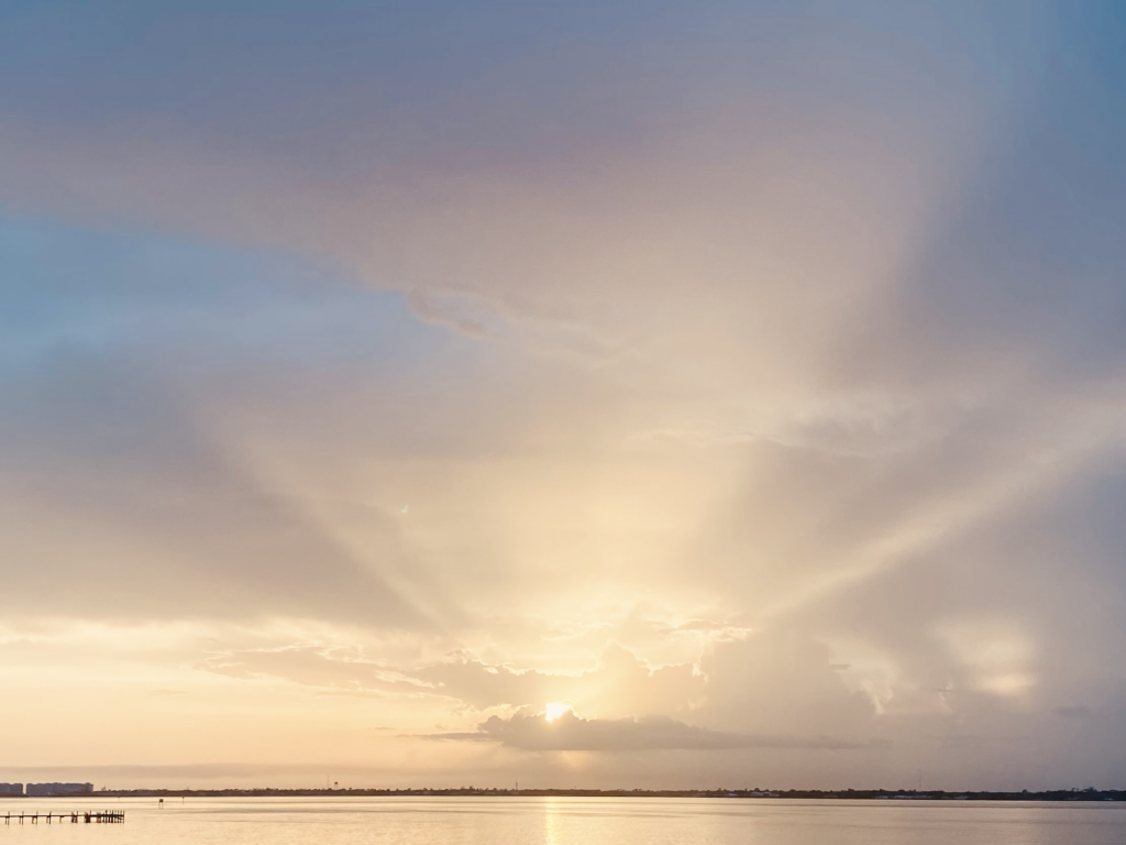 Sunrise background in Fort Myers Florida by the water with the sun coming through the clouds.
